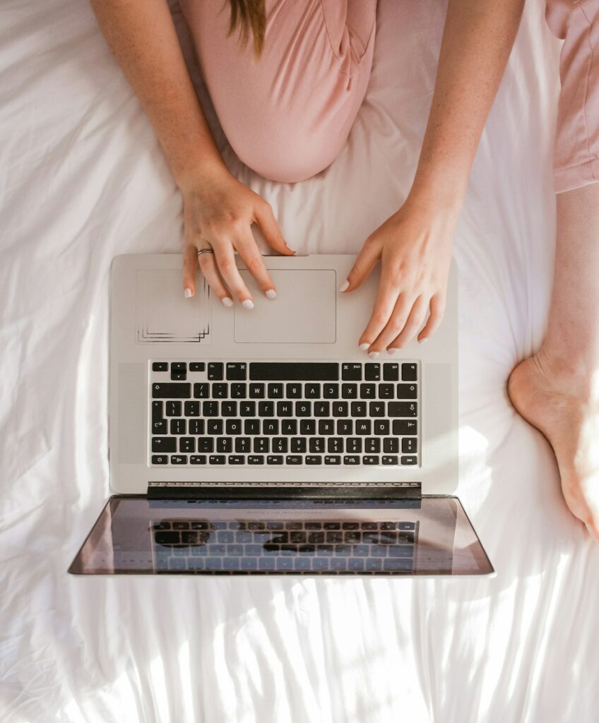 Top-down view of a person using a laptop on a white bedspread, representing the convenience and accessibility of our telehealth services for eating disorder support in Australia.