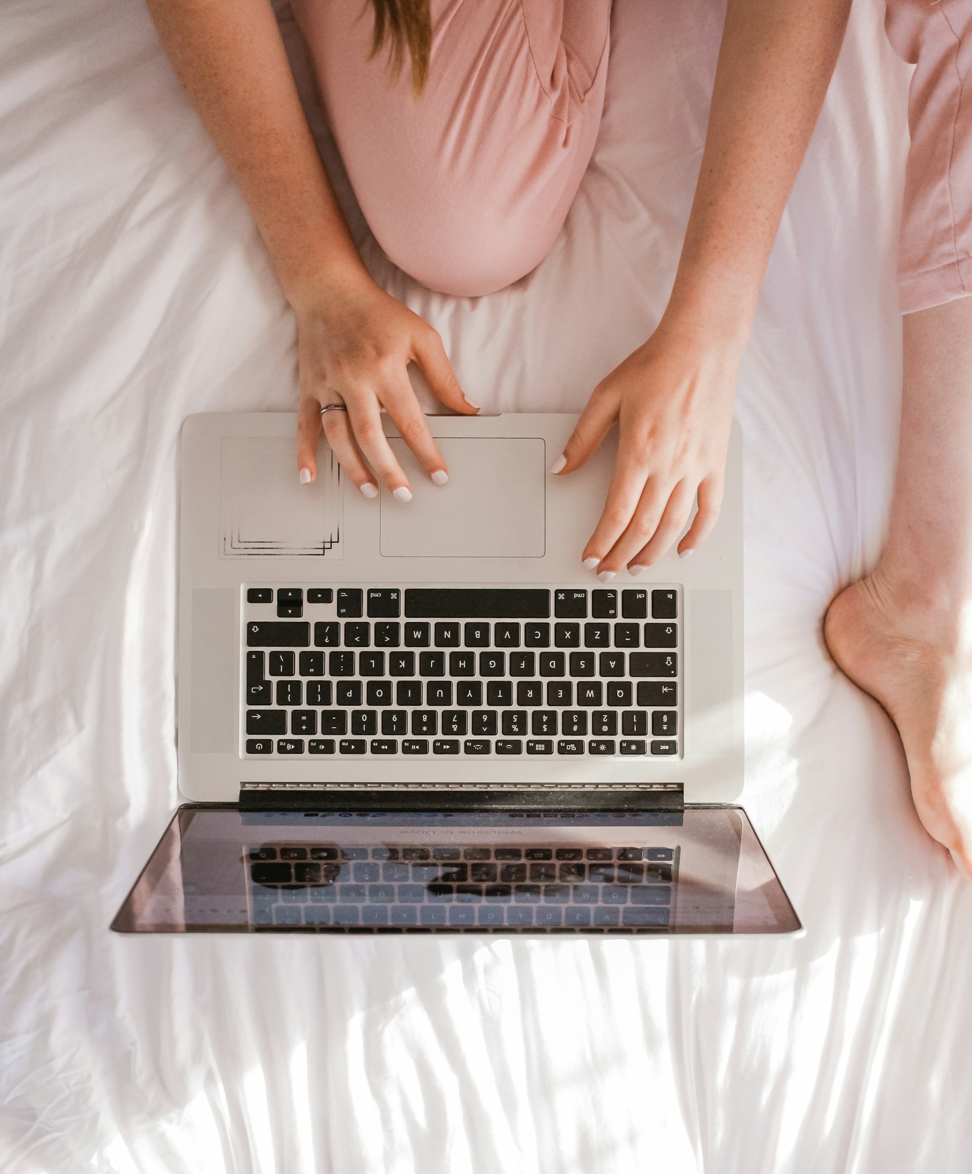 Top-down view of a person using a laptop on a white bedspread, representing the convenience and accessibility of our telehealth services for eating disorder support in Australia.