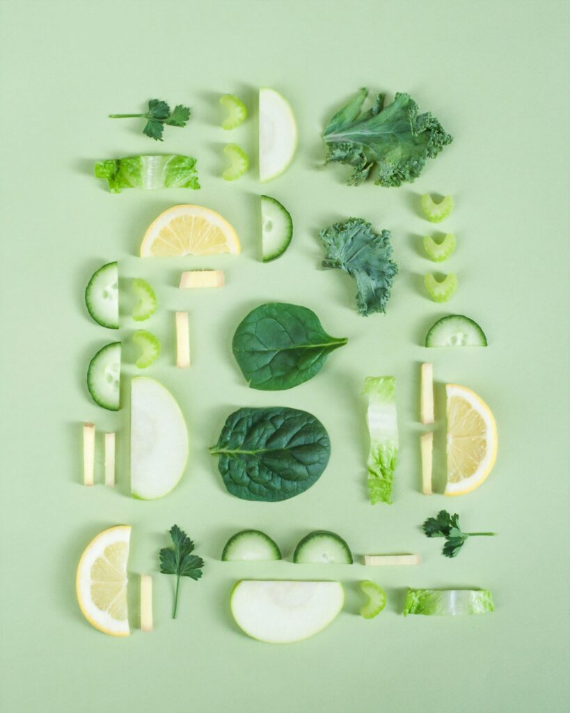 A variety of fresh, green vegetables and lemon slices artfully arranged on a pale green background, representing the balanced, nourishing dietary approach offered by our Hobart Eating Disorder Dietitian service.